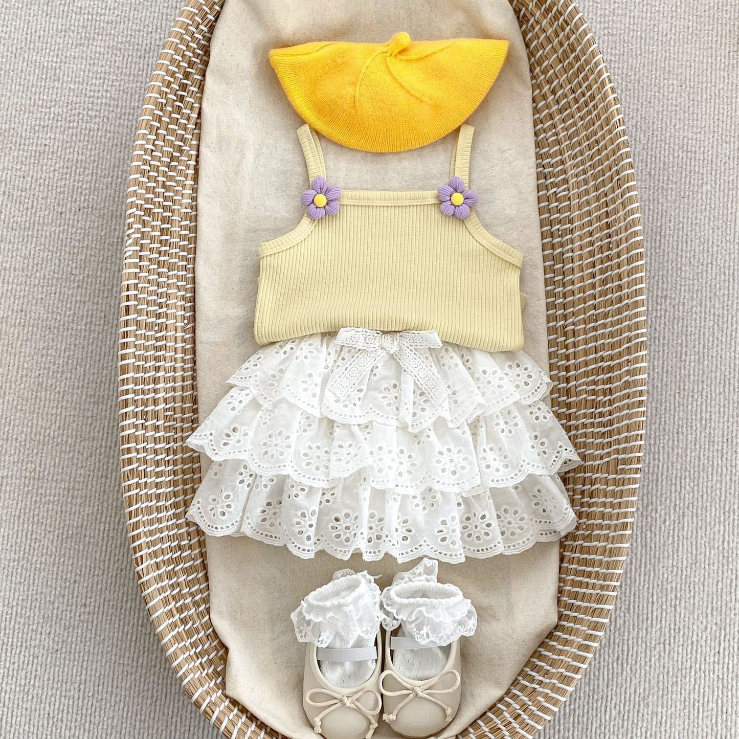 Children's outfit with yellow top, white lace skirt, and yellow hat on a textured surface.