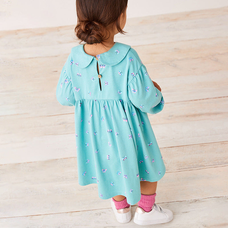 Child wearing a light blue dress with butterfly pattern on a wooden floor