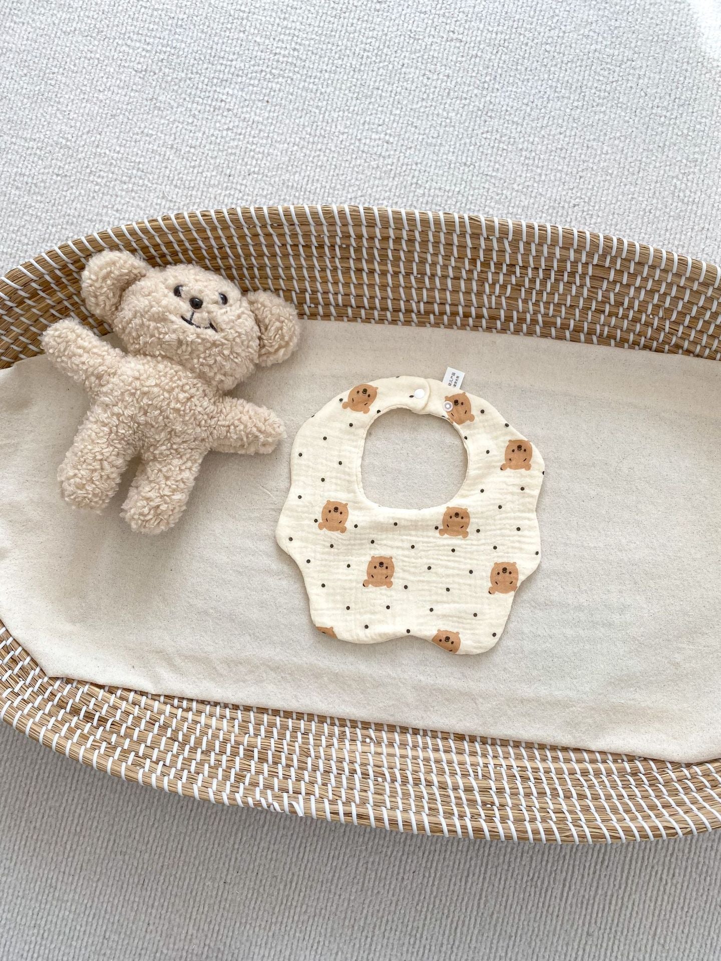 Baby bib and teddy bear in a woven basket on a light background