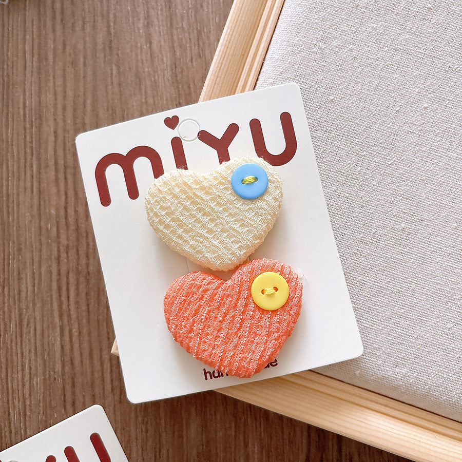 Heart-shaped hair clips on a Miyu branded card with a wooden surface background