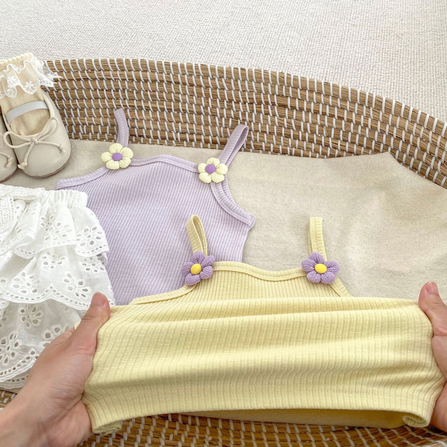 Yellow and purple children's dresses with floral straps on a textured surface.
