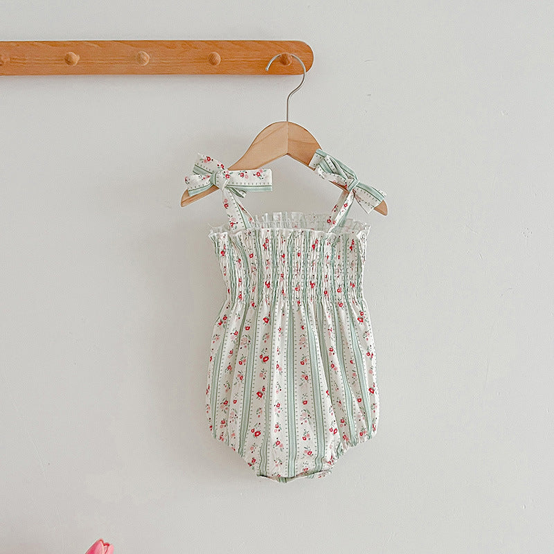 Floral baby romper with bow straps hanging on a wooden hanger against a light gray background