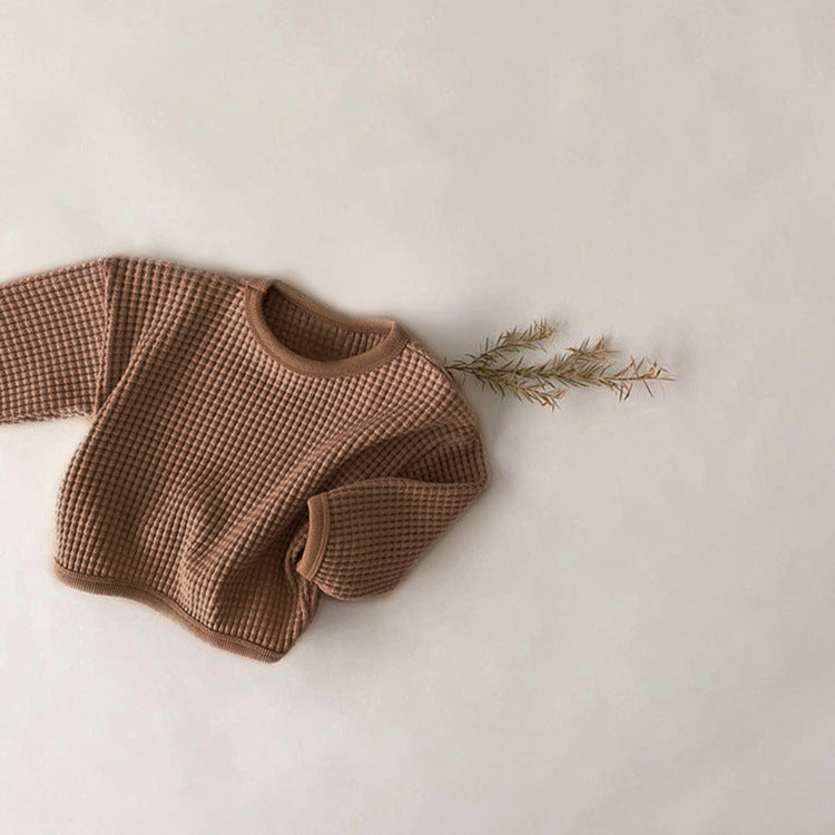 Brown textured sweater on a light beige background with a small branch.