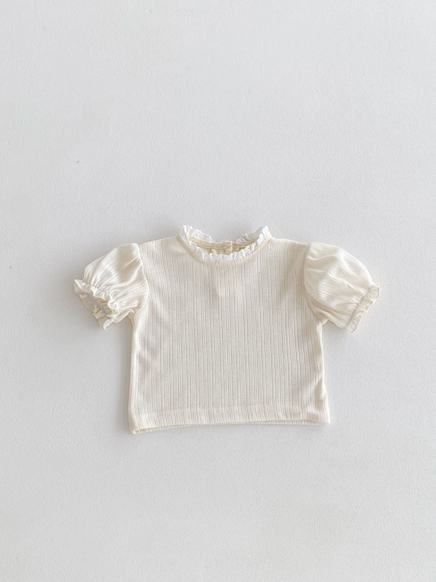 White ribbed blouse with ruffled sleeves on a light gray background