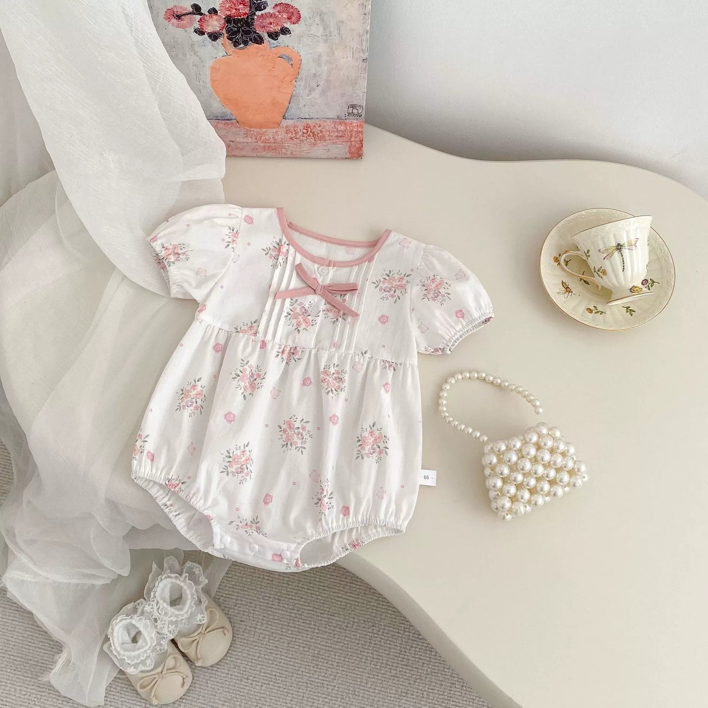 Baby romper with floral pattern on a white surface with decorative items.