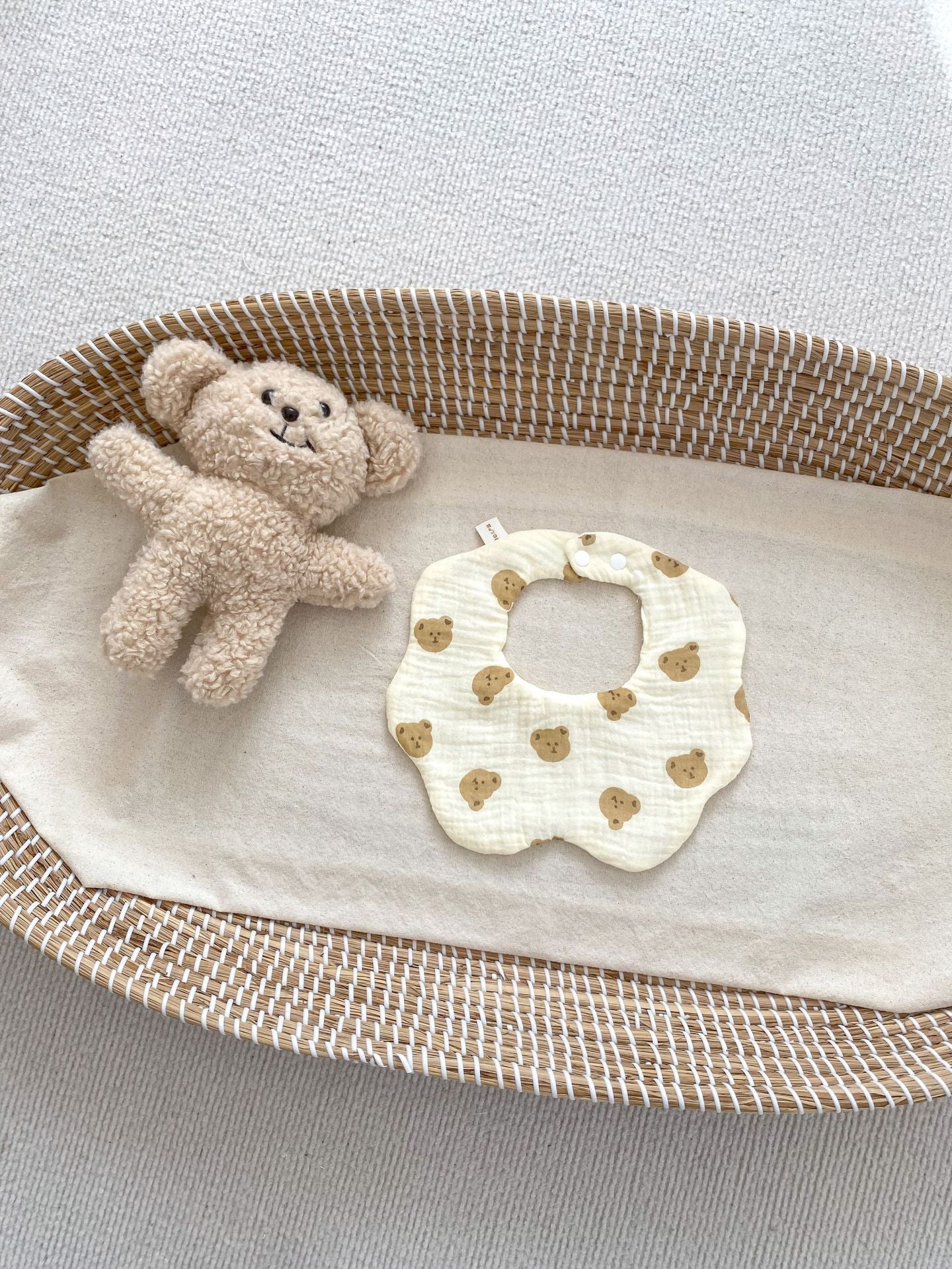 Baby bib with teddy bear design and small teddy bear in a basket on a light background