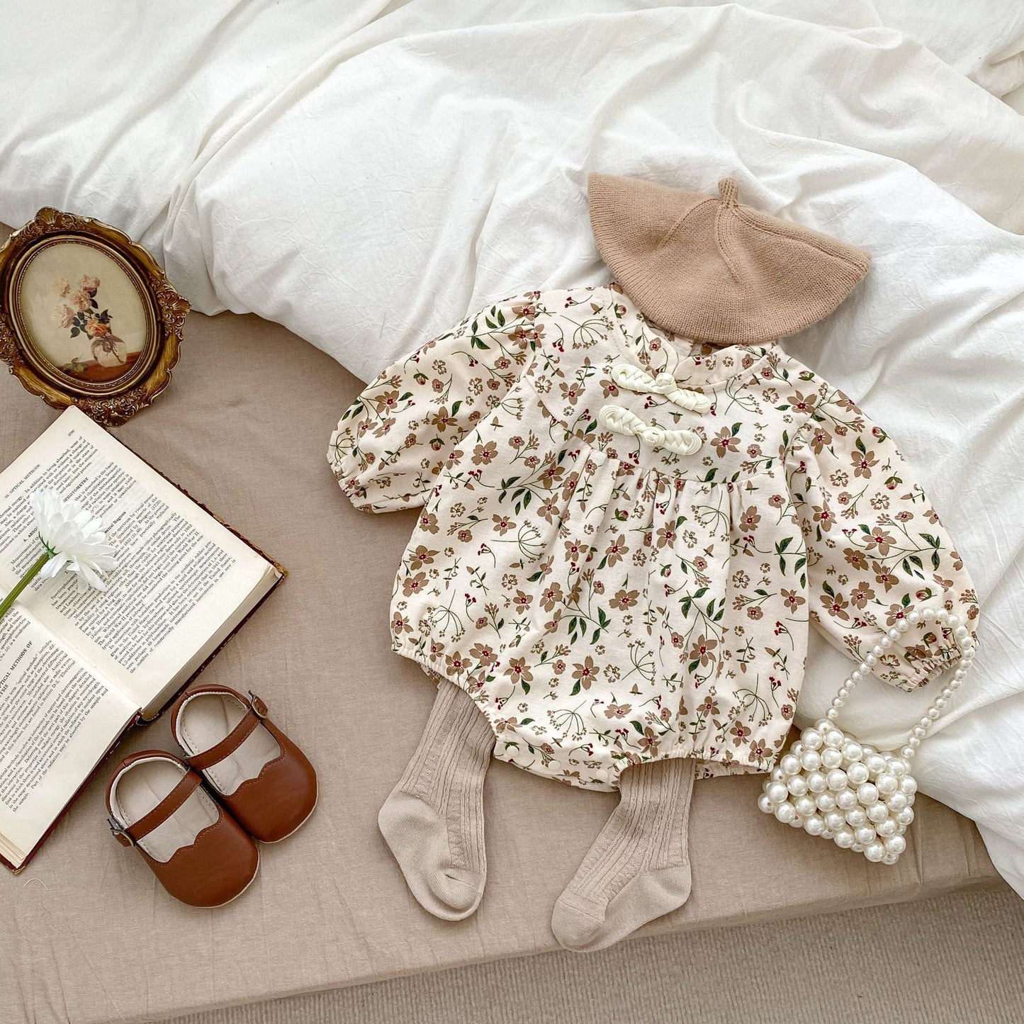Floral baby outfit with hat, shoes, and socks on a bed with an open book and decorative frame.