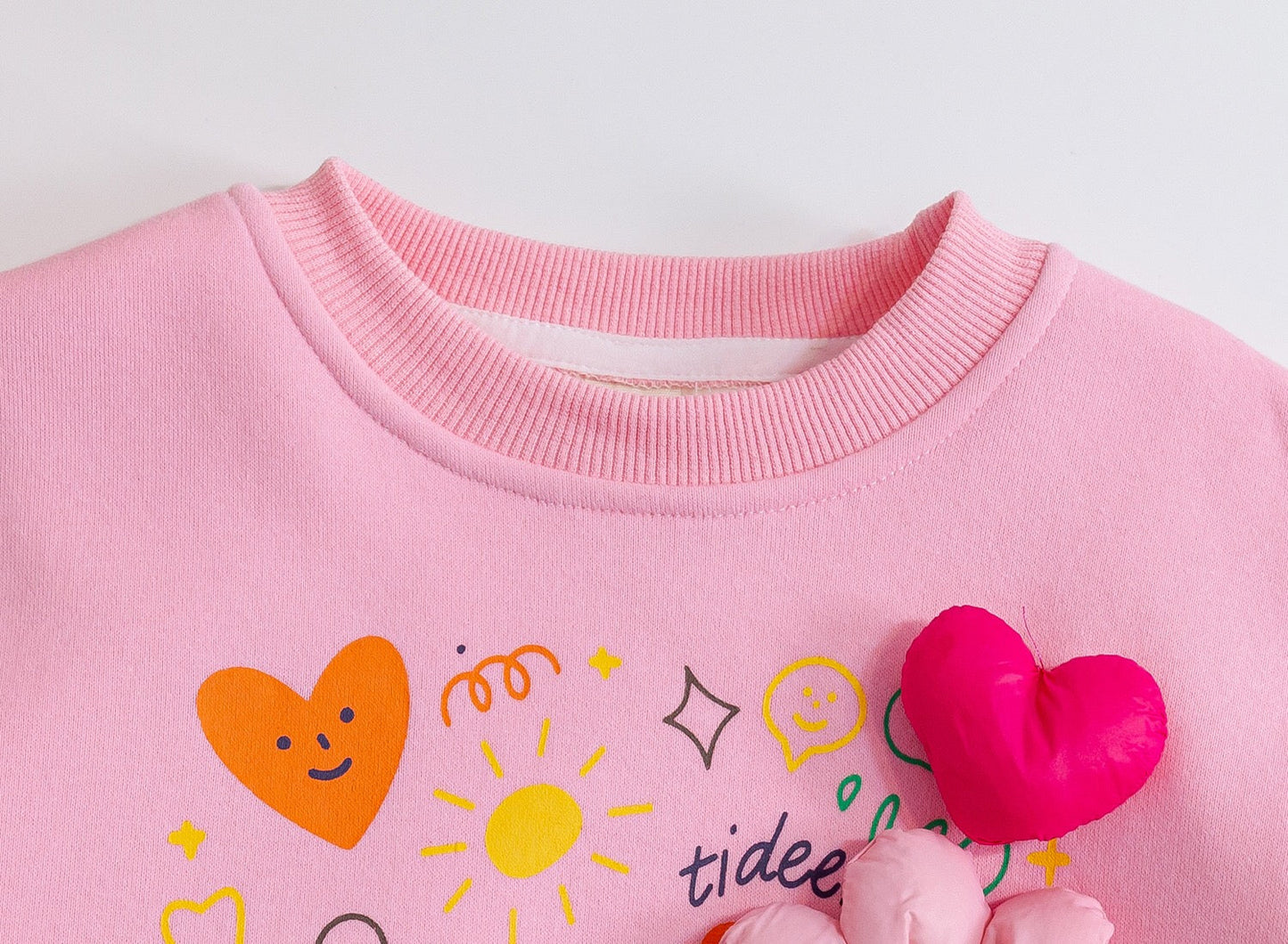Pink sweatshirt with colorful designs and a pink heart-shaped toy on a white background