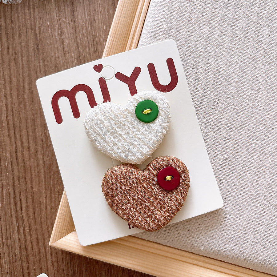 Heart-shaped hair clips on a Miyu branded card with a wooden surface and gray fabric background.