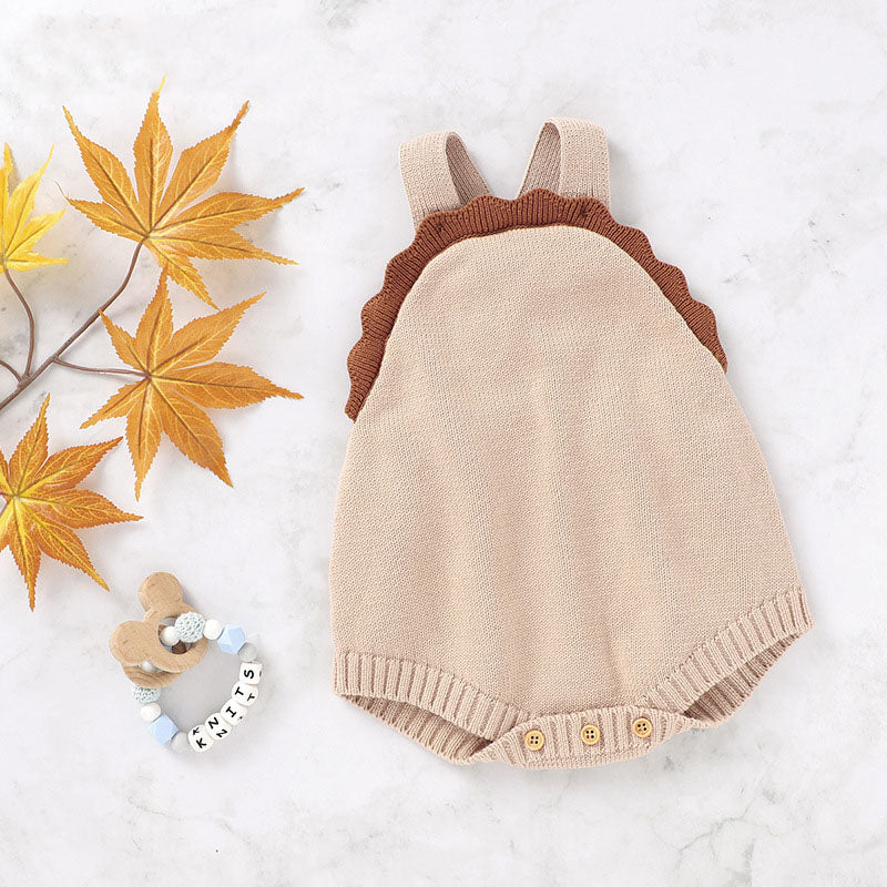 Beige baby romper with brown shoulder straps on a white background with autumn leaves.