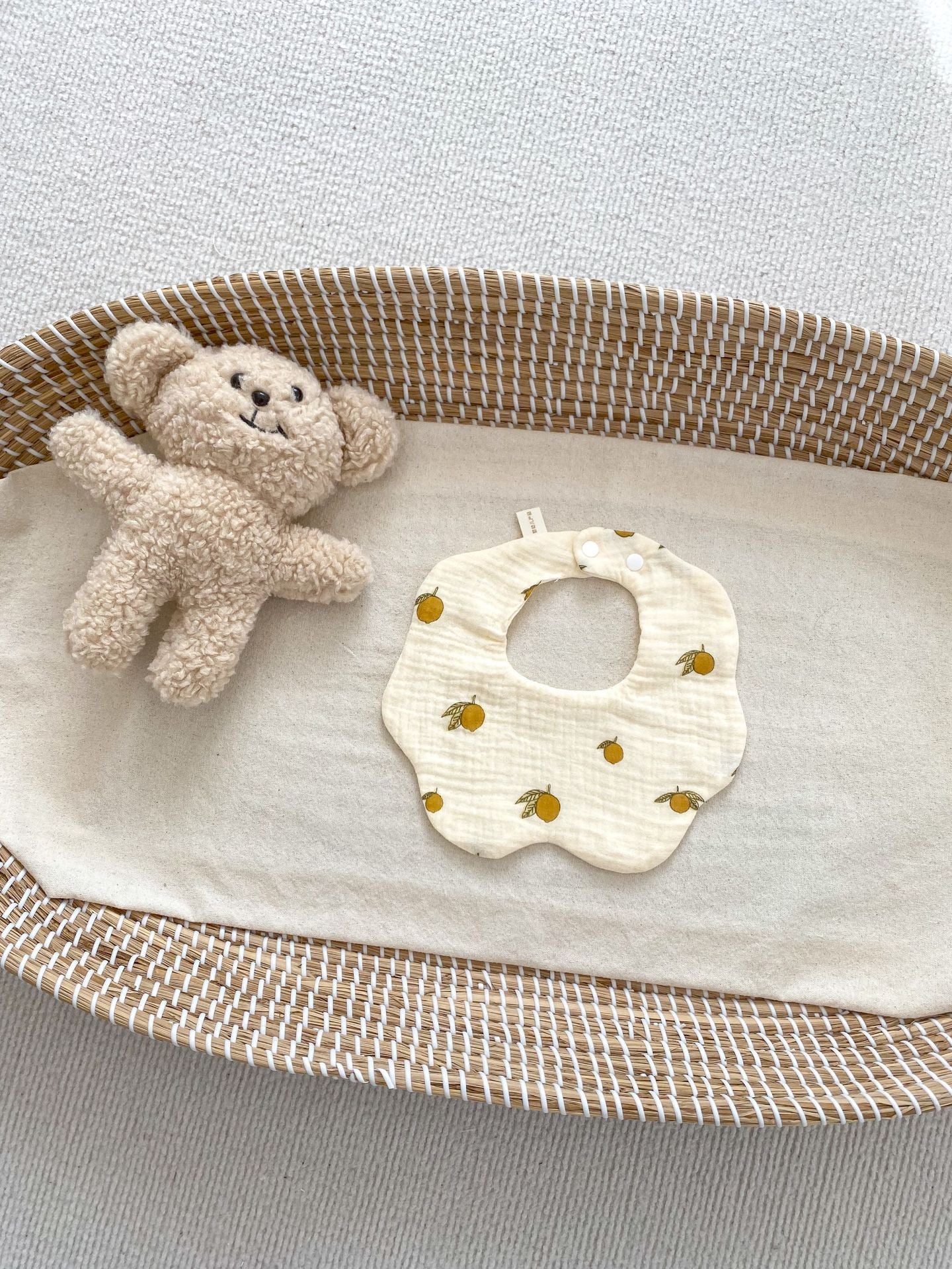 Baby bib and teddy bear in a crib with a light gray background