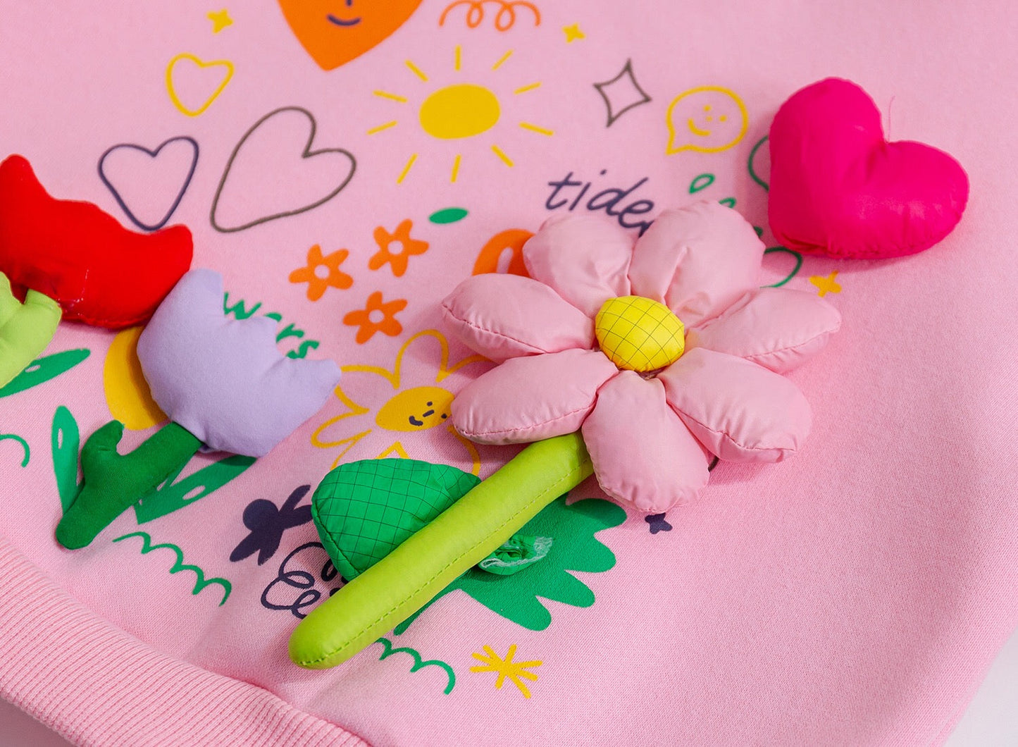 Pink flower-shaped plush toy on a pink blanket with colorful drawings