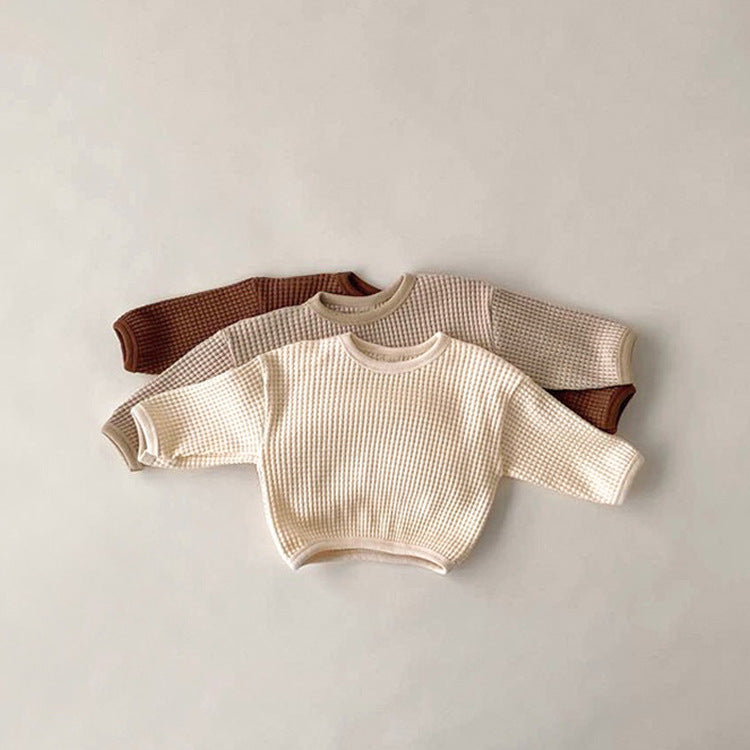 Two baby sweaters, one beige and one brown, on a light gray background