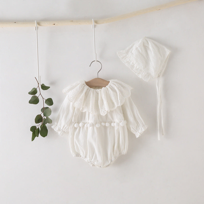 White baby romper with ruffles hanging on a wooden hanger against a white wall.