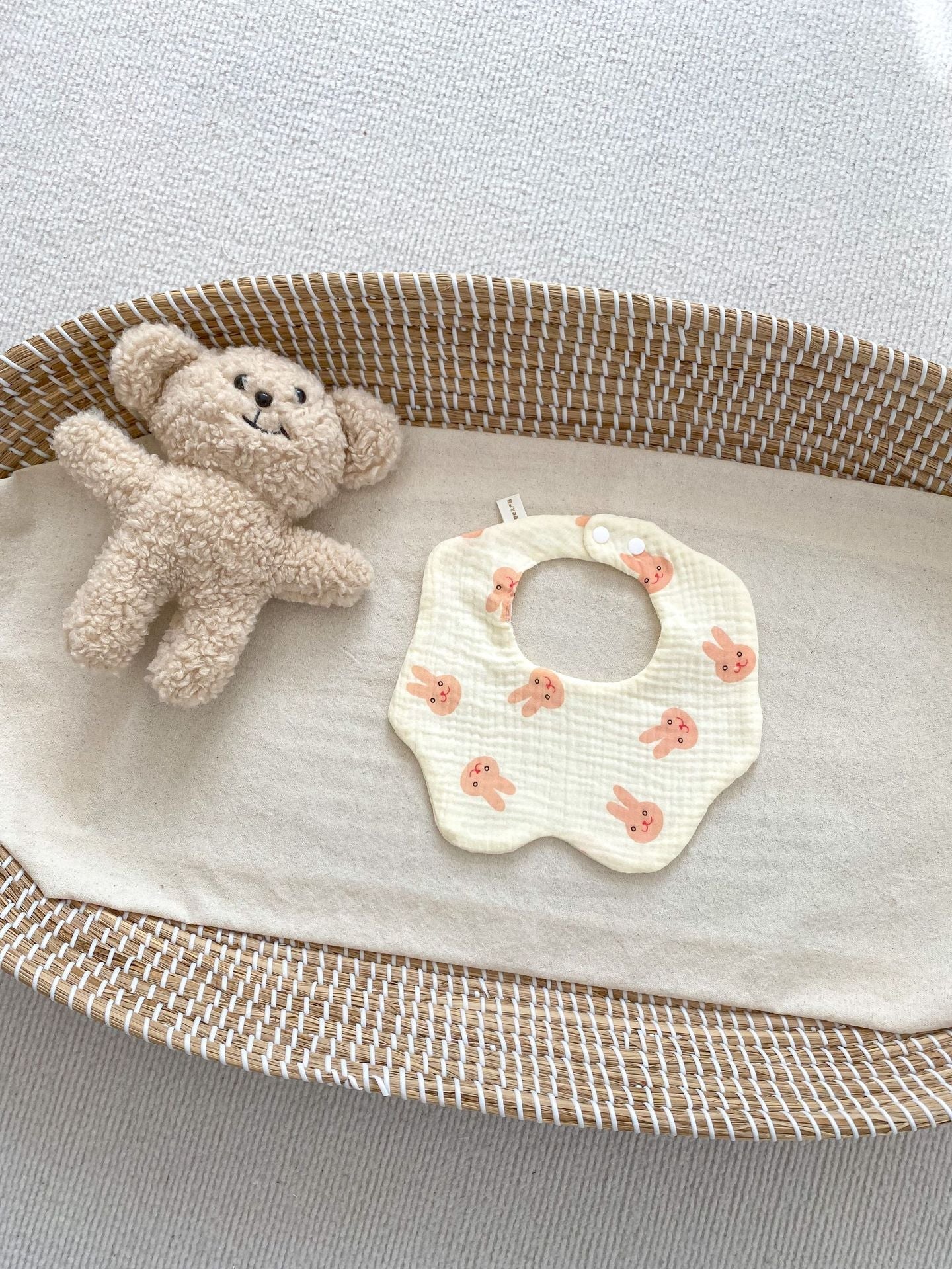 Baby bib with fish pattern and teddy bear in a crib on a light gray background