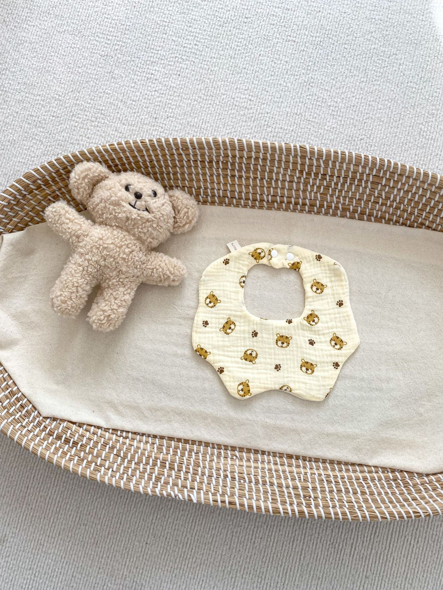 Baby bib with teddy bear design and small teddy bear in a woven basket on a light background