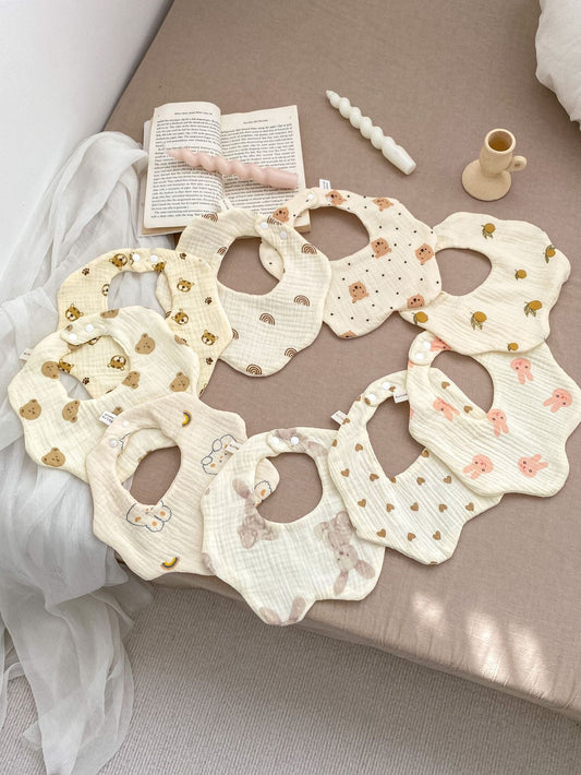 Set of baby bibs with floral patterns on a beige surface with a book and candle.