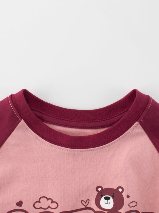 Close-up of a pink shirt with maroon sleeves and bear design on a white background