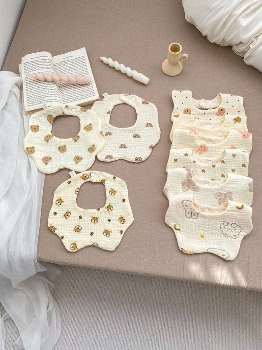 Baby bibs and onesie with floral patterns on a beige surface