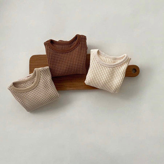 Three textured shirts in brown and beige on a wooden board against a light gray background