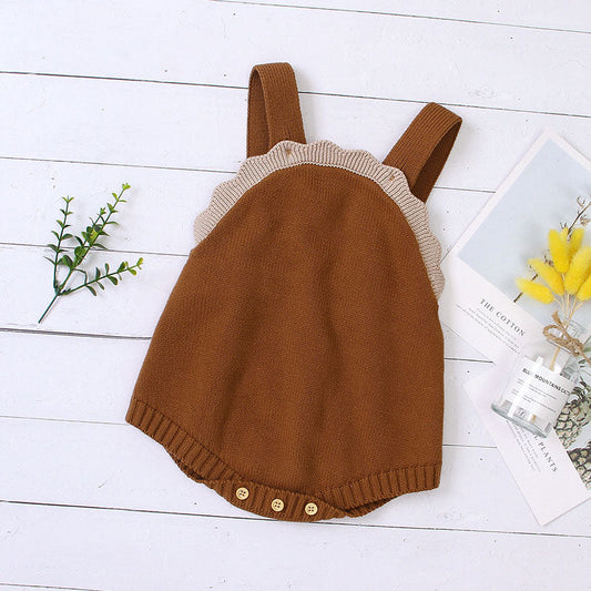 Brown knitted romper with ruffled neckline on a white wooden surface.