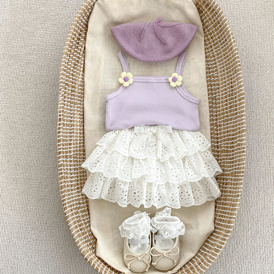 Children's outfit set with a purple top, white skirt, hat, and shoes displayed on a textured surface.