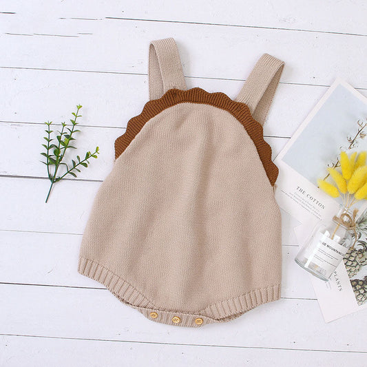 Beige knitted romper with brown scalloped edges on a white wooden surface.