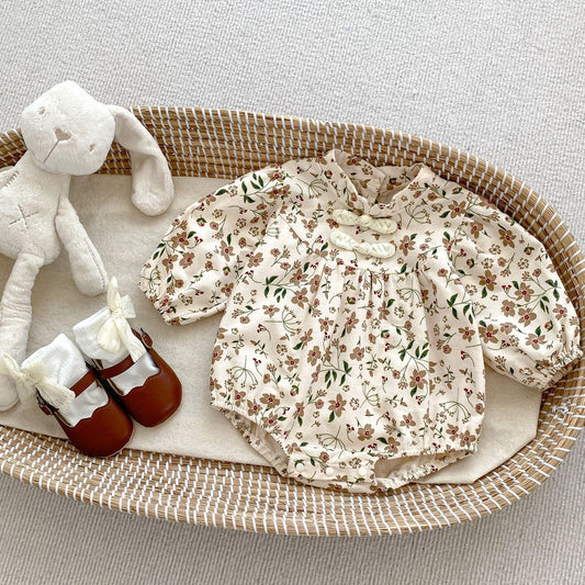 Floral baby outfit with shoes and stuffed toy on a woven tray