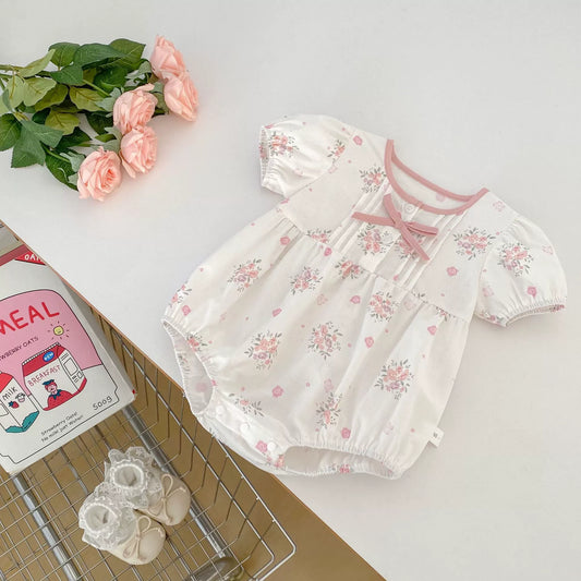 Floral baby romper with matching headband on a white surface with flowers and a book.