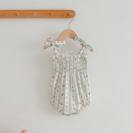 Floral baby romper with bow straps hanging on a wooden hanger against a light gray background