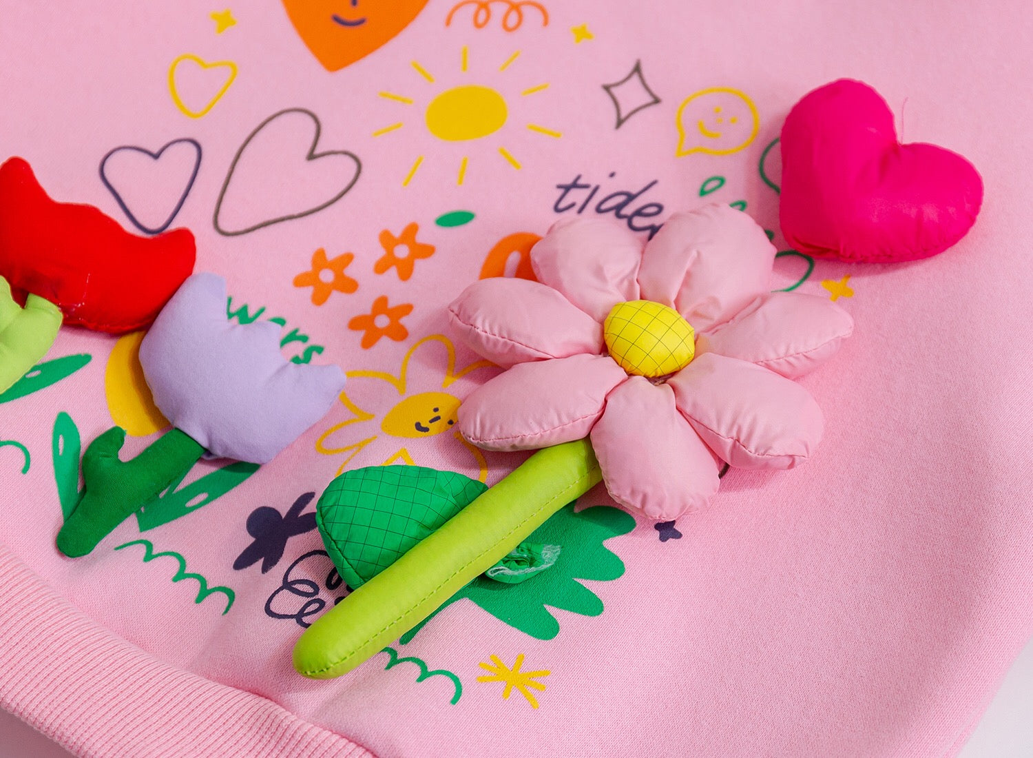Pink flower-shaped plush toy on a pink blanket with colorful drawings
