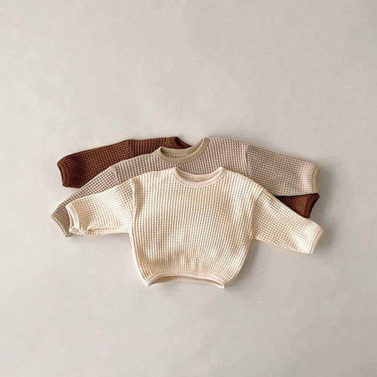 Two baby sweaters, one beige and one brown, on a light gray background