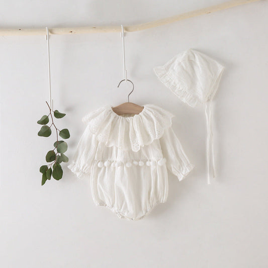 White baby romper with ruffles hanging on a wooden hanger against a white wall.